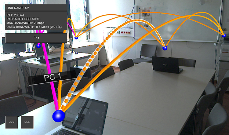 A photo of an AR network visualization with colored edges spanning between computers in the room.
